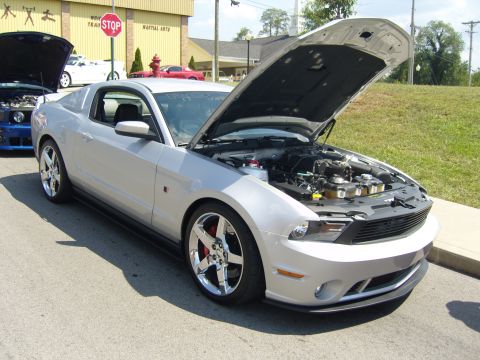 2007 Ford Mustang - A silver Ford Mustang is parked with its hood open, revealing the engine and chrome wheels. Another Mustang is visible in the background.
