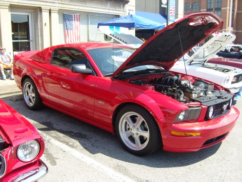 2007 Ford Mustang - A red 2007 Ford Mustang GT is parked with its hood open, showing the engine, alongside other vehicles.