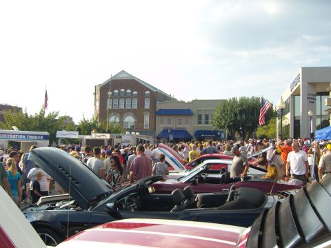 2007 Ford Mustang - Convertible Mustangs on display at a car show with many spectators and buildings in the background.