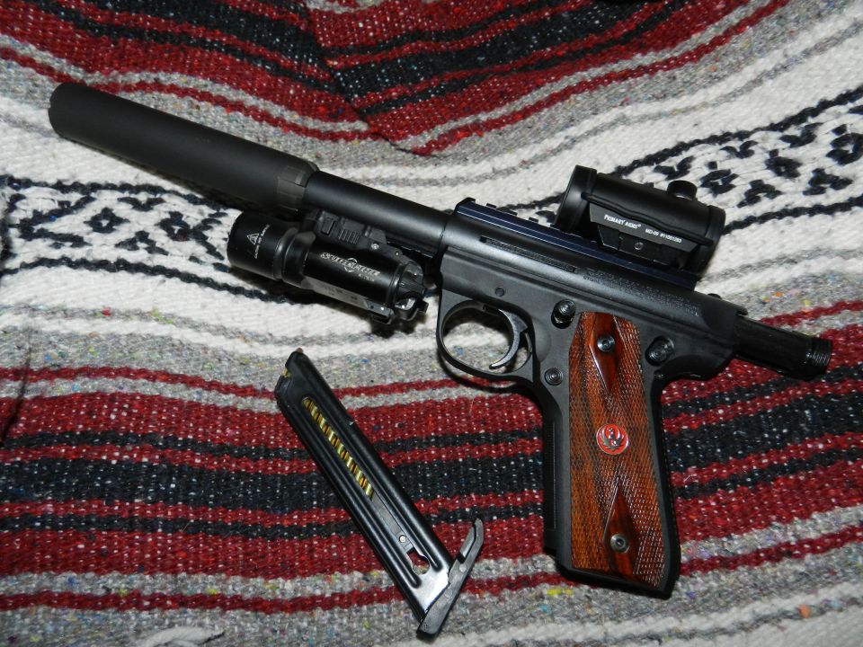 Pistol with suppressor, SureFire flashlight, and Aimpoint red dot sight, next to a loaded magazine