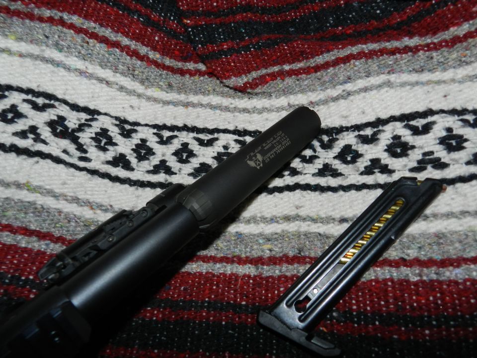 Gun with suppressor and loaded magazine on a blanket. Text on suppressor is visible