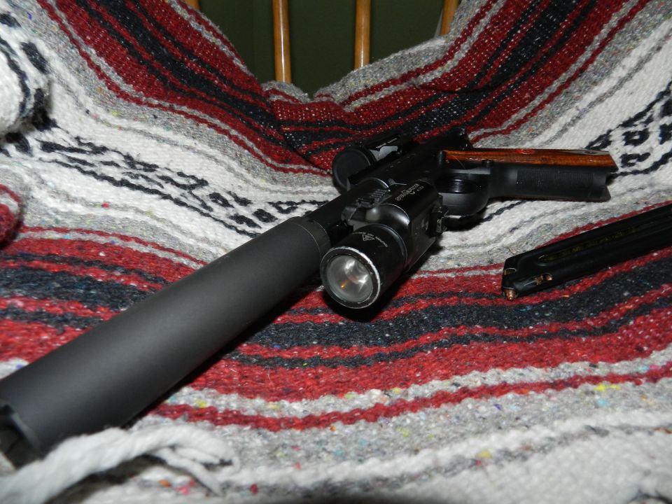 Handgun with suppressor, flashlight, and magazine on a striped blanket