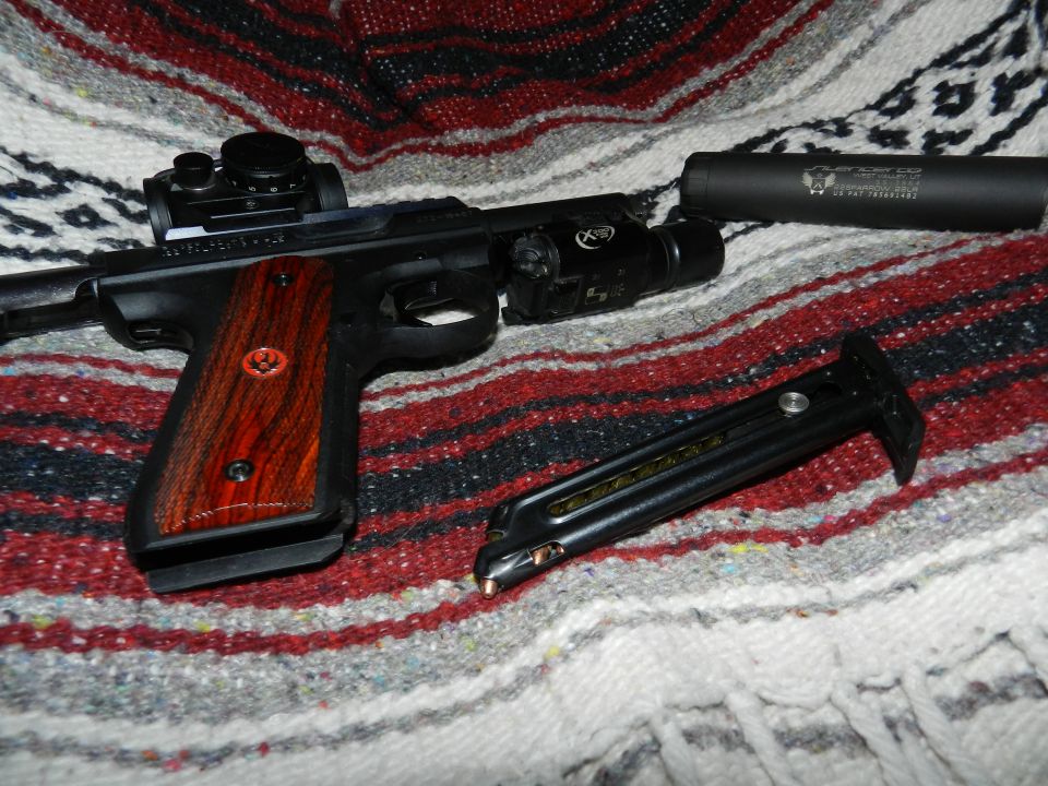 Pistol with red dot sight, laser, and suppressor, next to a magazine