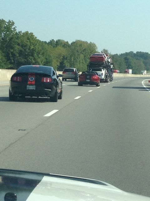 2007 Ford Mustang - A black 2007 Ford Mustang with red racing stripes is seen on the highway, followed by other vehicles including a car carrier.