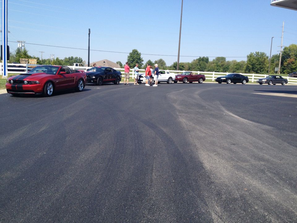 Red Ford Mustang convertible with black racing stripes, parked on asphalt
