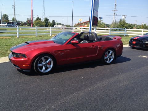 2007 Ford Mustang - A red 2007 Ford Mustang GT convertible with black racing stripes is parked next to another Mustang at a car show.