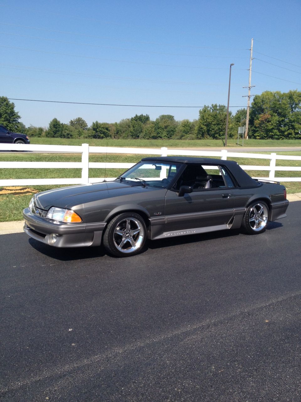 Gray convertible Mustang with black top and chrome wheels parked on asphalt