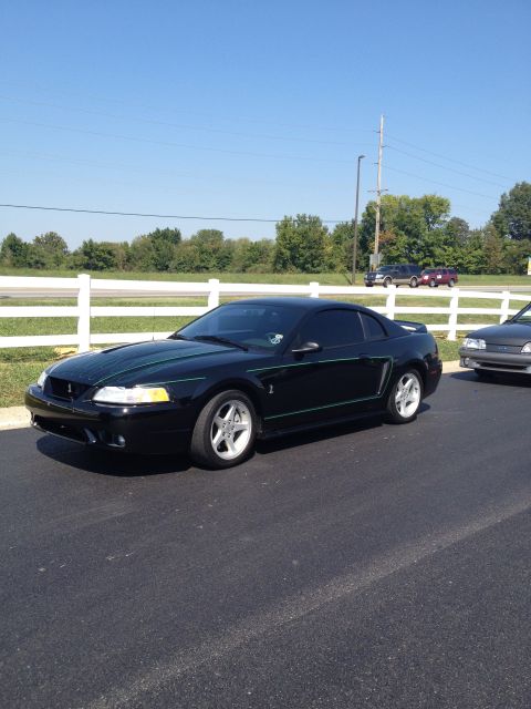 2007 Ford Mustang - A black Ford Mustang with green racing stripes is parked on asphalt next to a white fence.