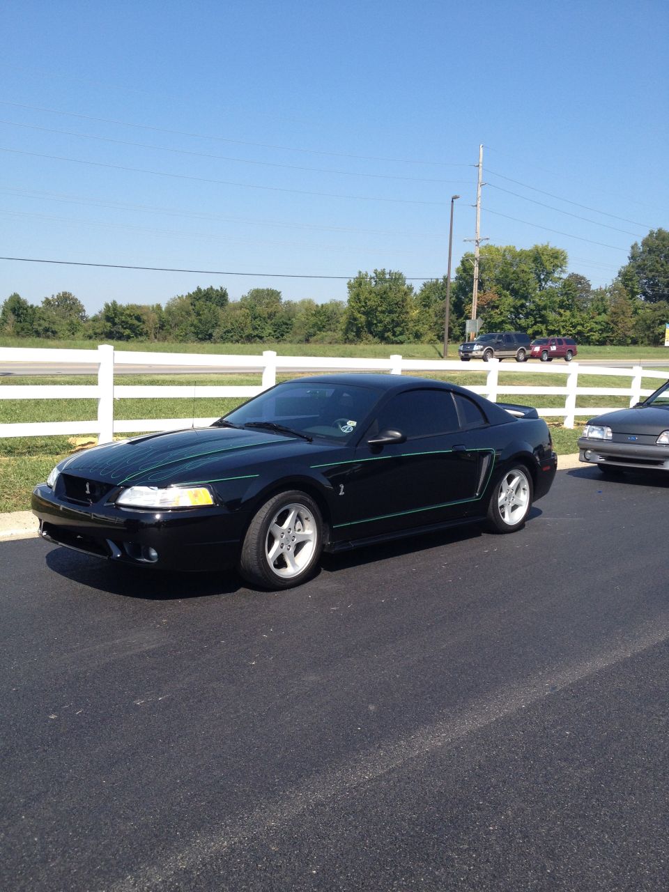 Black Ford Mustang with green stripes parked next to another car. It has a spoiler and aftermarket wheels