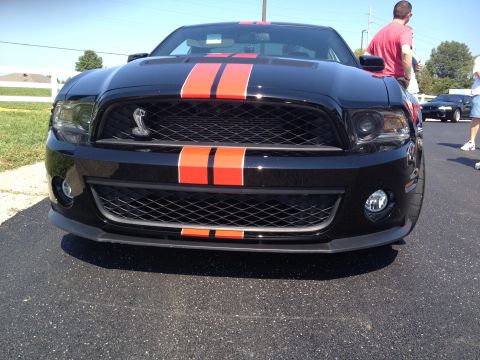 2007 Ford Mustang - A black Ford Mustang with prominent orange racing stripes is parked on asphalt, with people nearby.