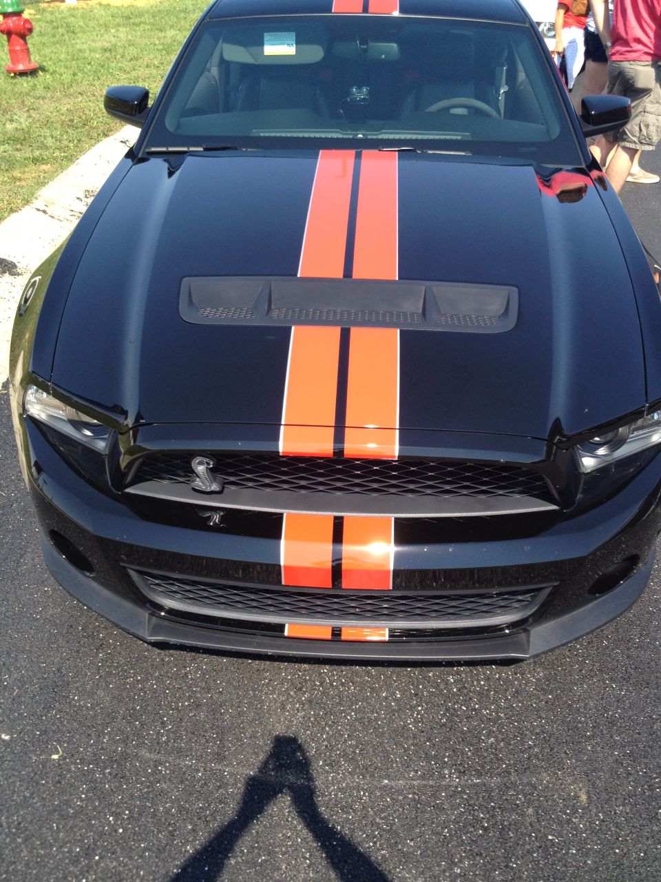 Black Ford Mustang with orange racing stripes, front view, showing grille and hood scoop