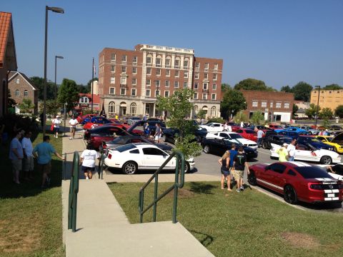 2007 Ford Mustang - A red Ford Mustang with white racing stripes is parked at a car show, with many other vehicles visible in the background.