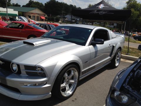2007 Ford Mustang - A silver 2007 Ford Mustang is parked at a car show, with a Mustang branded tent in the background.