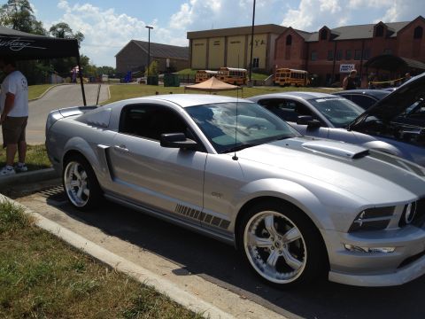 2007 Ford Mustang - A silver 2007 Ford Mustang is parked at an outdoor event, with other vehicles and buildings visible.