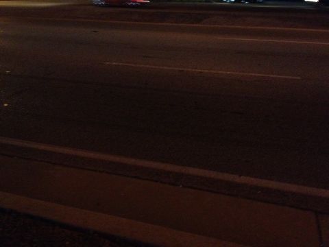 2007 Ford Mustang - A dark, blurry photo shows a street at night with a curb and road lines visible.