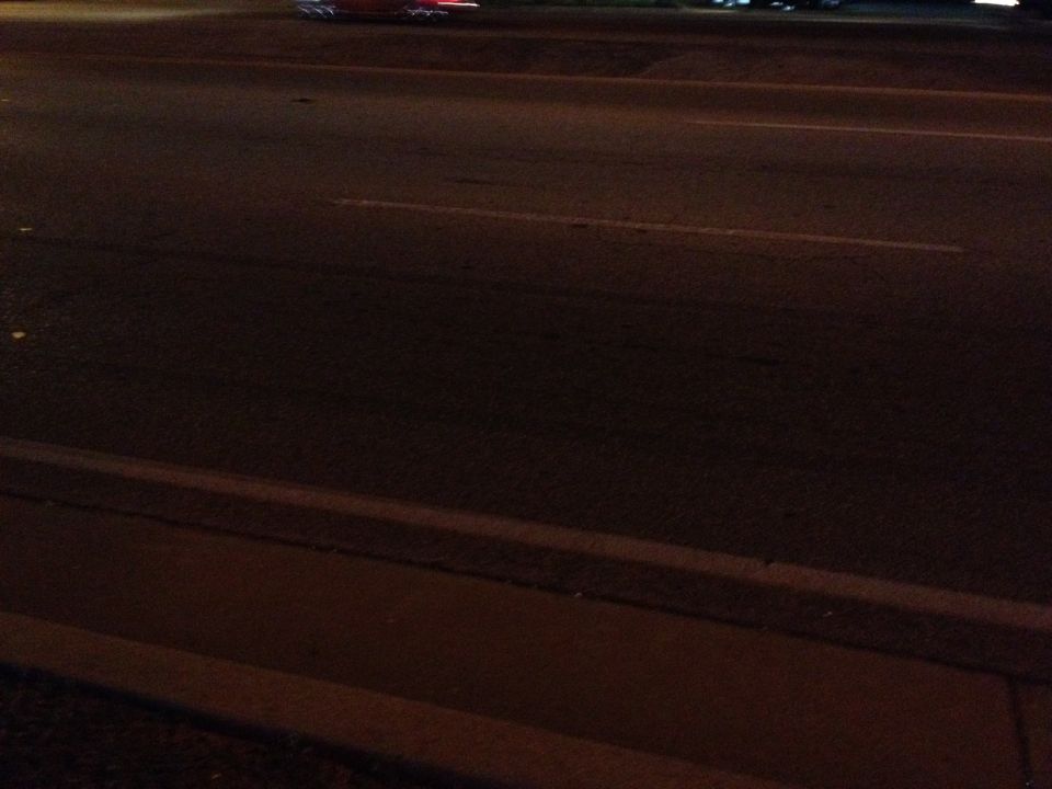 night shot of a street with a curb and road markings, some lights in the distance
