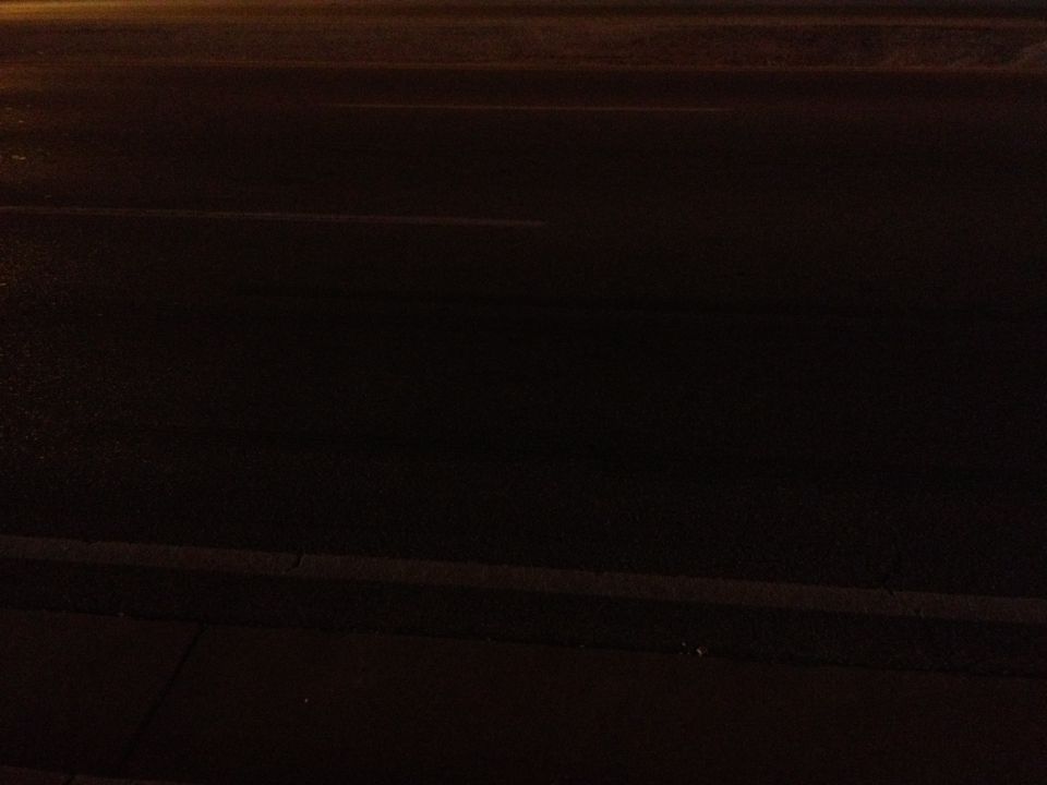 Dark asphalt road with faint yellow lines and a concrete curb at night