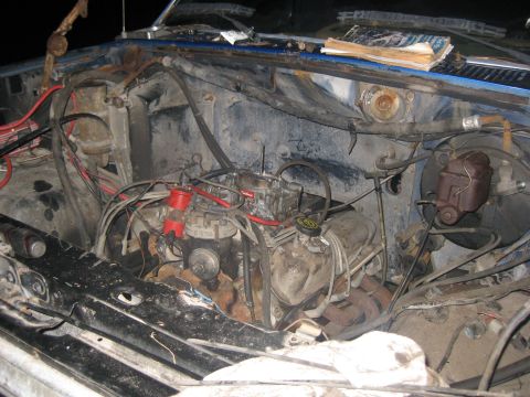 1994 Ford Bronco - The engine bay of a blue vehicle shows a carburetor and distributor, with some books on the dashboard.