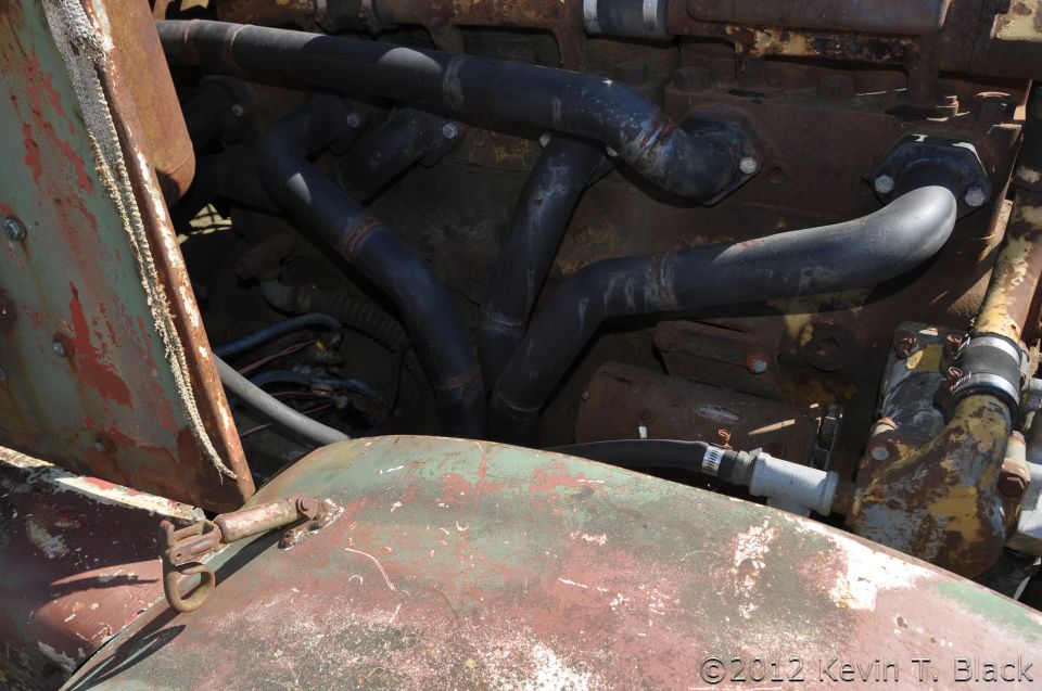 Close-up of a rusty engine compartment showing black hoses and pipes, with green and red painted metal parts