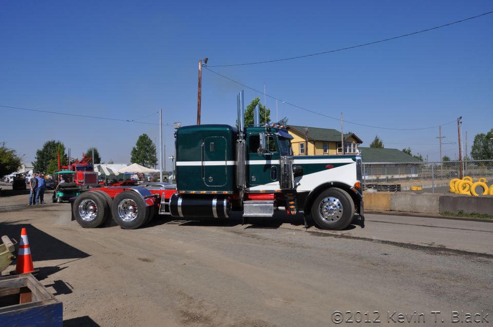 Green and white semi-truck, side view. Other trucks and tents in background