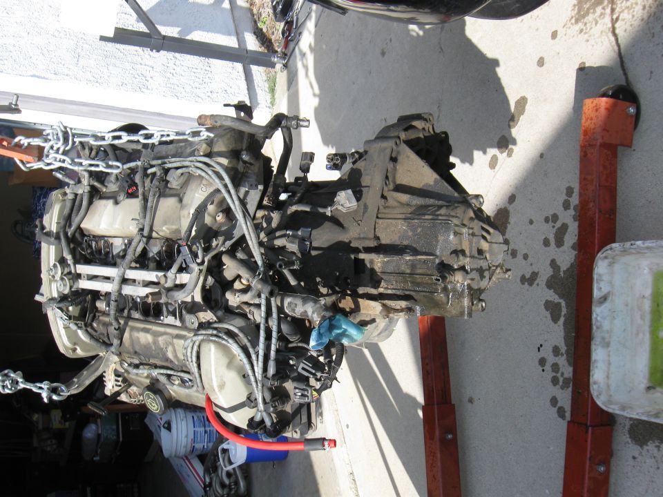 Engine and transmission assembly suspended by chains, resting on engine stands