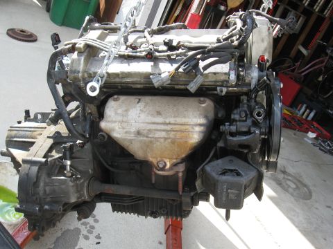 1992 Ford Taurus - This engine assembly, likely removed from a vehicle, is being supported by chains and a red stand.