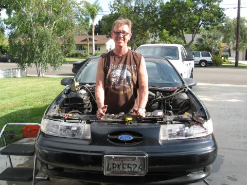 1992 Ford Taurus - A man stands in front of a black 1992 Ford Taurus with its hood open, revealing the engine compartment.