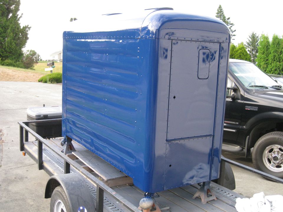 Blue truck sleeper cab on a trailer, next to a black pickup truck