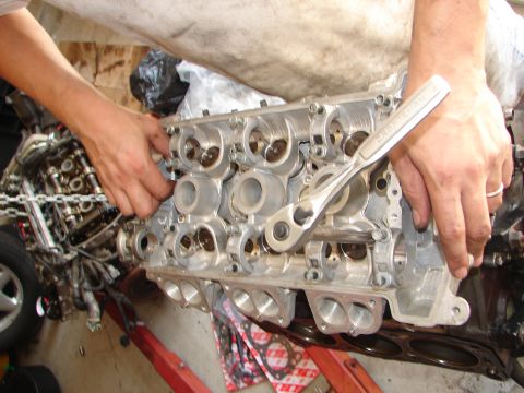 1992 Ford Taurus - Mechanic's hands are shown working on a vehicle's engine cylinder head, using a ratchet tool.