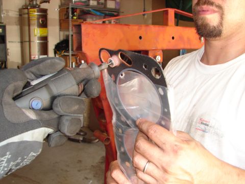 1992 Ford Taurus - A person uses a rotary tool to modify an engine gasket in a garage setting.