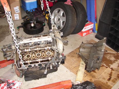 1992 Ford Taurus - Engine and transmission components are laid out on the floor, with tires and an oil pan nearby.