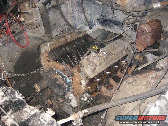 Engine bay with V8 engine, hoses, and wiring visible. Some parts appear rusty