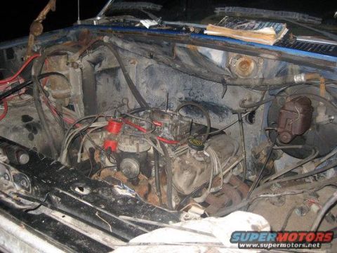 1985 Ford Bronco - The engine bay of a blue vehicle shows a V8 engine with a carburetor and extensive wiring, indicating a need for maintenance.