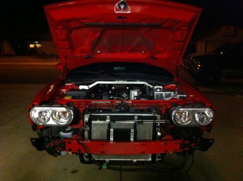 2010 Dodge Challenger - Front view of a red 2010 Dodge Challenger with the hood open and front bumper removed, revealing the engine and radiator.