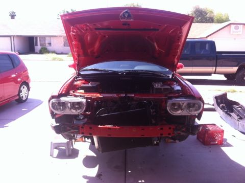 2010 Dodge Challenger - Front end of a red Dodge Challenger undergoing repairs, hood open, bumper removed.