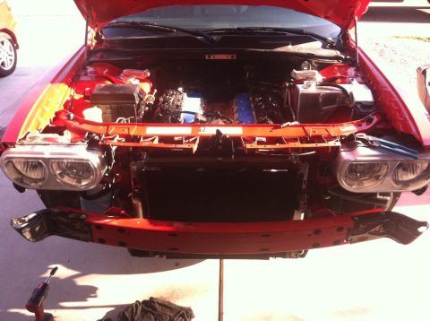 2010 Dodge Challenger - The front end of a Dodge Challenger is shown with the hood up and the engine exposed, indicating recent work or disassembly.