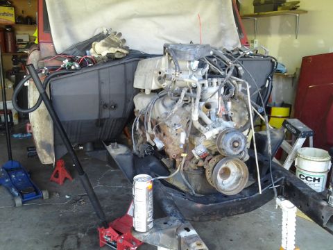 1968 Ford Bronco - The engine bay of a vehicle is shown with the V8 engine exposed, supported by jack stands and a floor jack.