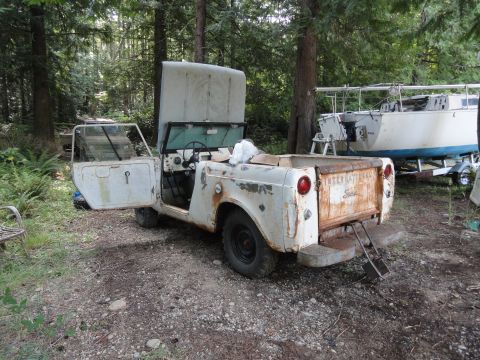 1962 International Scout 80 - This weathered International pickup truck, likely from the early 1960s, sits in a forest clearing with its hood and doors ajar.