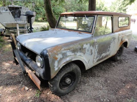 1962 International Scout 80 - This weathered SUV sits outdoors, showing significant rust and peeling paint, with a boat and trailer visible behind it.