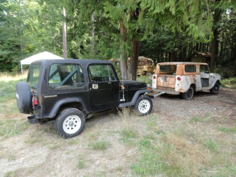 1962 International Scout 80 - A vintage 1962 International Scout 80, showing significant rust, is towed by a black Jeep Wrangler in a wooded area.