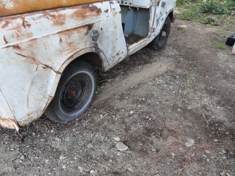1962 International Scout 80 - The weathered body of an old truck shows significant rust and wear, with its door ajar, parked on a rough outdoor surface.