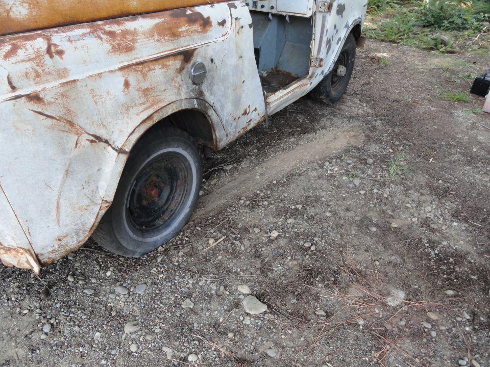 Side view of a rusty, weathered truck with the door open, sitting on a dirt and gravel surface