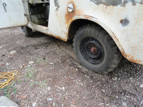 1962 International Scout 80 - This weathered off-road vehicle sits with its door ajar and a flat tire, showing signs of age and disuse.