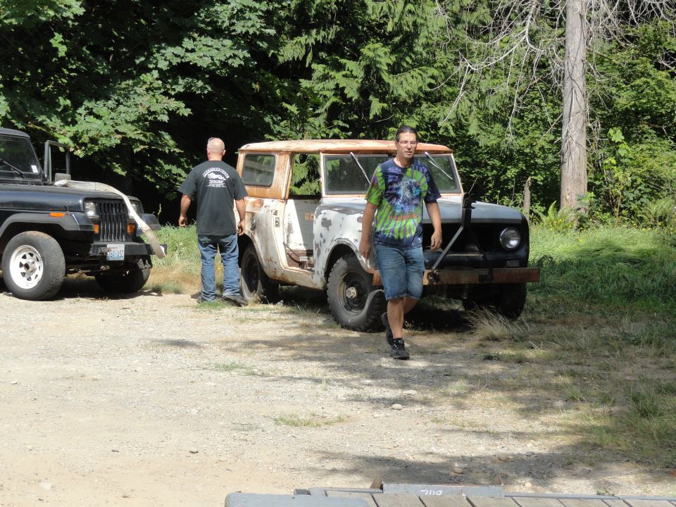 White International Scout with rusty roof and black grille, parked on gravel lot next to a black Jeep