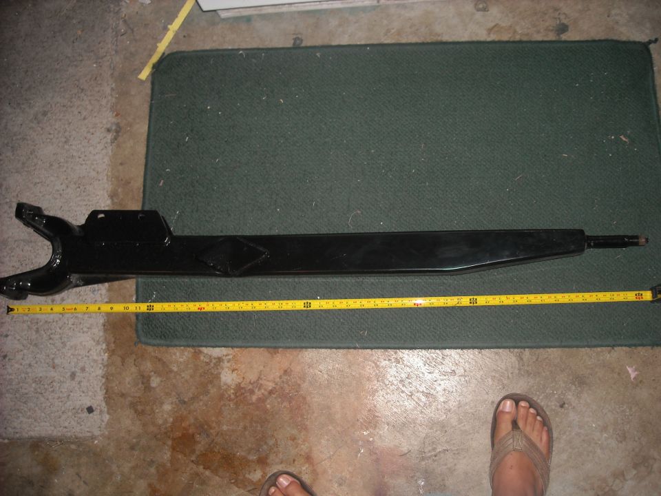 Black metal automotive suspension component with a yellow measuring tape laid alongside it