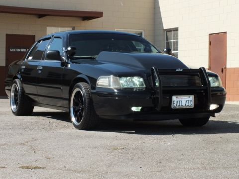 2003 Ford Crown Victoria - Lowered Crown Victoria on black wheels with brush guard parked by a Custom Mfg Co. building.
