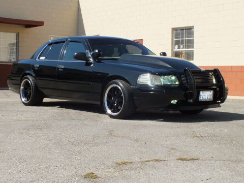 2003 Ford Crown Victoria - Black Crown Victoria at a front angle shows brush guard, fog lights and chrome-lip wheels.