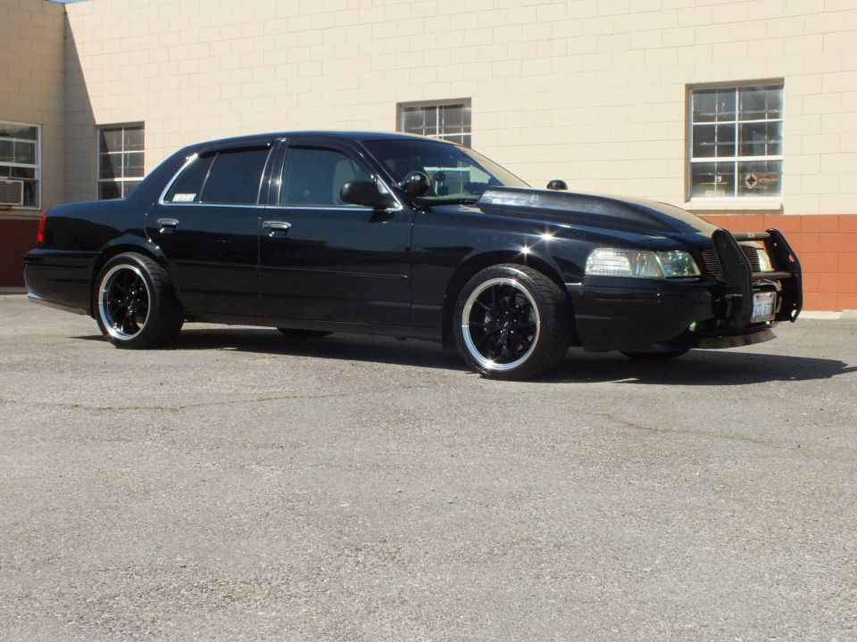 Black Ford sedan front three-quarter with push bar and chrome-lip wheels in lot