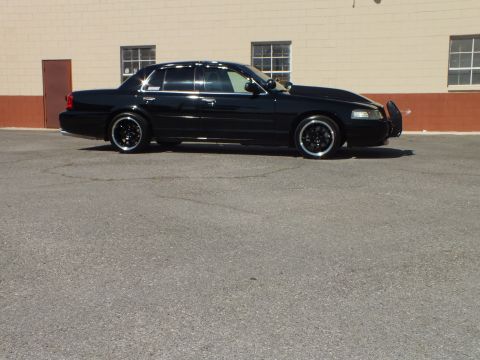 2003 Ford Crown Victoria - Side profile of a lowered black sedan on chrome-lip wheels beside a building with windows.