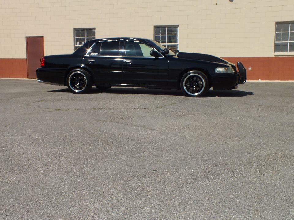 Black Ford sedan side profile on chrome-lip wheels parked by building windows